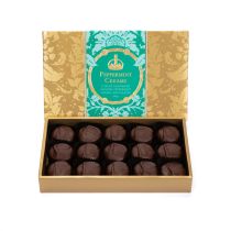 A box of Peppermint Creams with gold embossed Acanthus packaging and a blue band with "Peppermint Creams: Luxury Handmade Peppermint Cream Chocolates." Lid of the box is postioned above the tray of dark chocolate Peppermint Creams. 