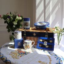 Coronation Hamper featuring biscuit tin, chocolates, two mugs and tea caddy on tea towel with decorated with flowers. 