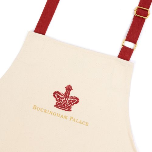 Cream coloured apron with deep red adjustable straps and large central pocket, red crown with Buckingham Palace spelled out in golden thread at the top centre. 