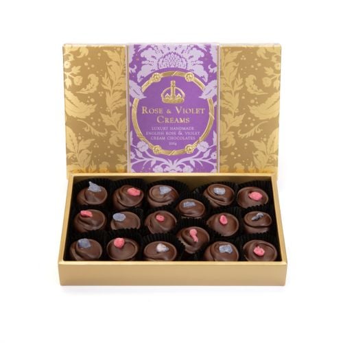 A box of Rose & Violet Creams with gold embossed Acanthus packaging and a purple band with "Rose & Violet Creams: Luxury Handmade English Rose & Violet Cream Chocolates." 