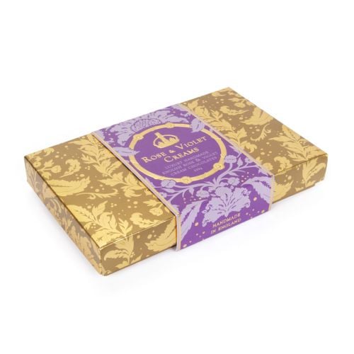 A box of Rose & Violet Creams with gold embossed Acanthus packaging and a purple band with "Rose & Violet Creams: Luxury Handmade English Rose & Violet Cream Chocolates." 