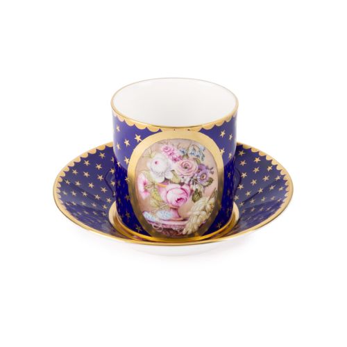 The Prestige Basket of Flowers Gobelet Litron, featuring central oval shape with hand painted bouquet of pink, purple and white flowers in a vase. The rest of the teacup and saucer has a rich cobalt blue paint and is finished with 22 carat gold gilding al