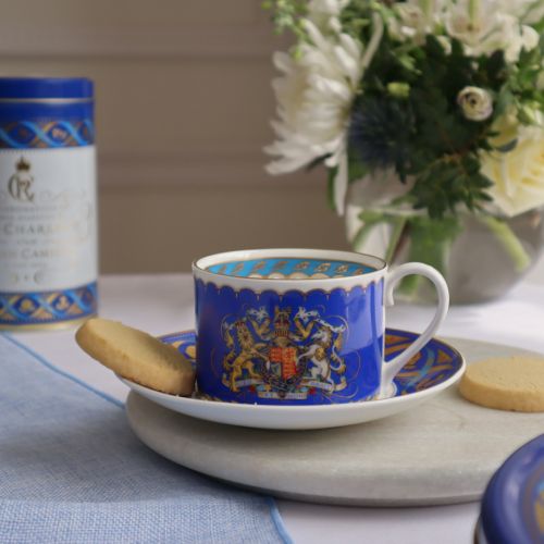 Teacup and saucer. Blue with white handle and gold accents. Royal coat of arms at the centre of the teacup.