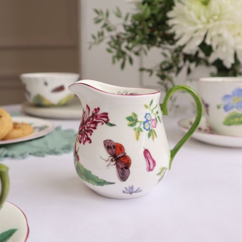 White milk jug with painted flowers and green handle. 