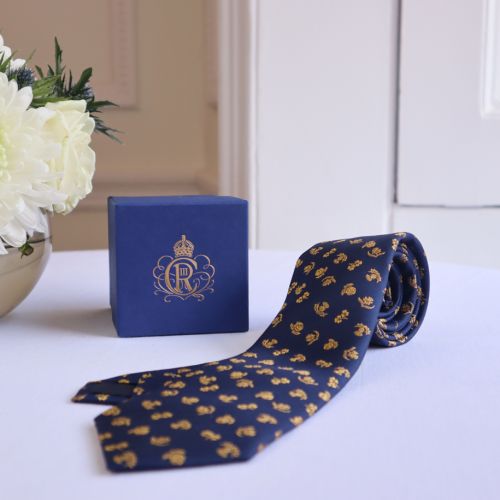 Close up image of our 100% woven silk tie in navy blue and burnished gold with floral motifs from the four nations of the United Kingdom -  thistle, rose, shamrock and daffodil . 