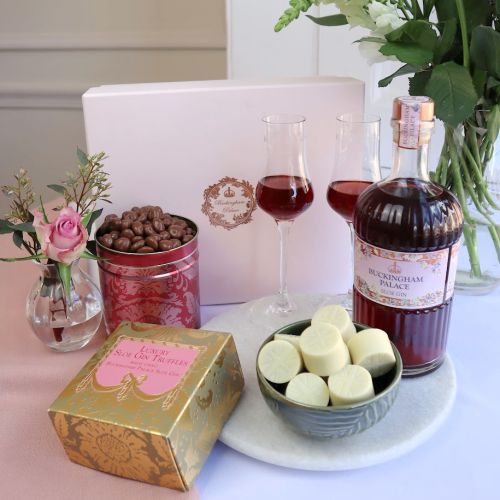 The Sloe Gin & Sweet Treats Gift Box with a pink gift box with Buckingham Palace in the background, a pink tin with chocolate raisins , a Buckingham pPalace Sloe Gin Bottle and Luxury Sloe Gin Truffles with white chocolate in a green bowl with the box to 