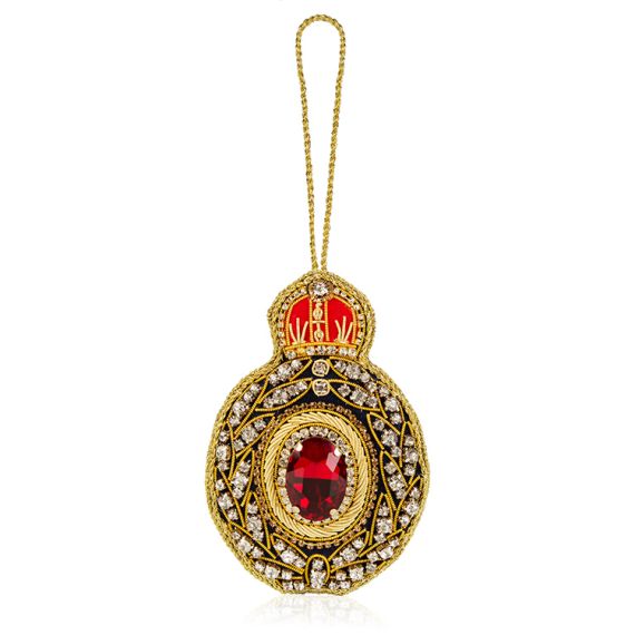 Black oval decoration with gold embroidery and clear crystals. Large, oval red crystal at the centre and topped with embroidered red crown. 