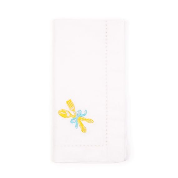 A folded white cotton napkin with fork and spoon embroidered in the corner, tied with a pretty blue bow 