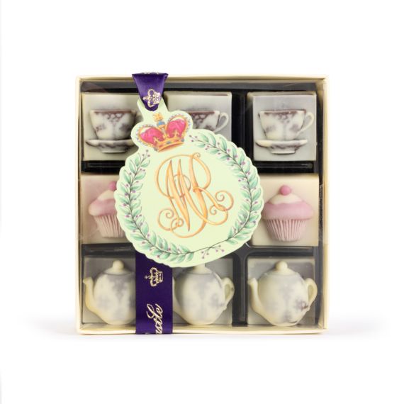 A square chocolate box with a clear lid featuring nine small individual chocolates with three unique rows of chocolates with the following designs, teacup and saucer, a cupcake and a teapot. Finished with a purple ribbon with gold crowns and the insignia 