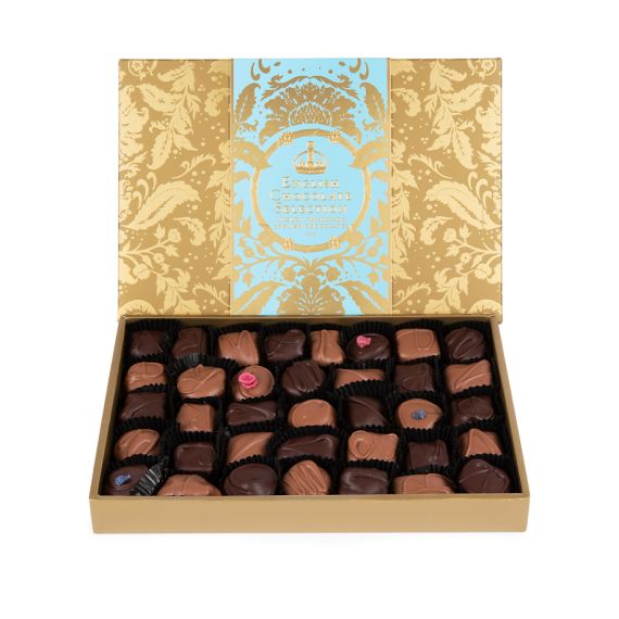 A side angle of the box of English Truffles with gold embossed Acanthus packaging and a light blue band with "English Truffles: Luxury Handmade English Chocolates." The tray of mixed chocolates are positioned at the bottom, with violet and English rose cr