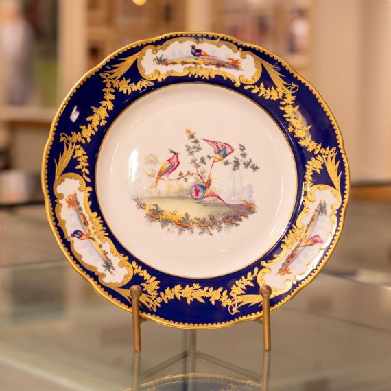 Image of the Prestige Sevres Cobalt Plate on stand, featuring three exotic birds at centre and cobalt blue edging with detailing. 