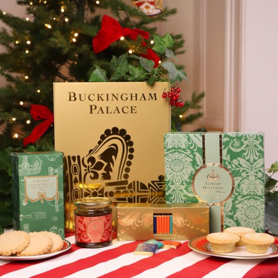 Buckingham Palace Gold Gift Box with a selection of festive treats set against a Christmas tree on a red and white striped tablecloth. 