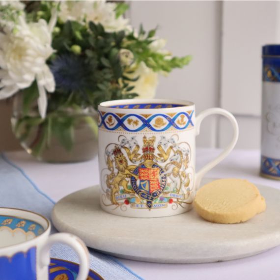 White coffee mug with Royal coat of arms, blue ribbon and national flowers in gold round the rim.