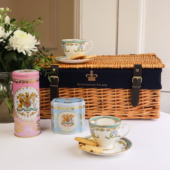 A wicker hamper with two Great Exhibition tea cups, a pink biscuit tin and a blue Earl Grey Tea Caddy. There are flowers to the left of this image. 