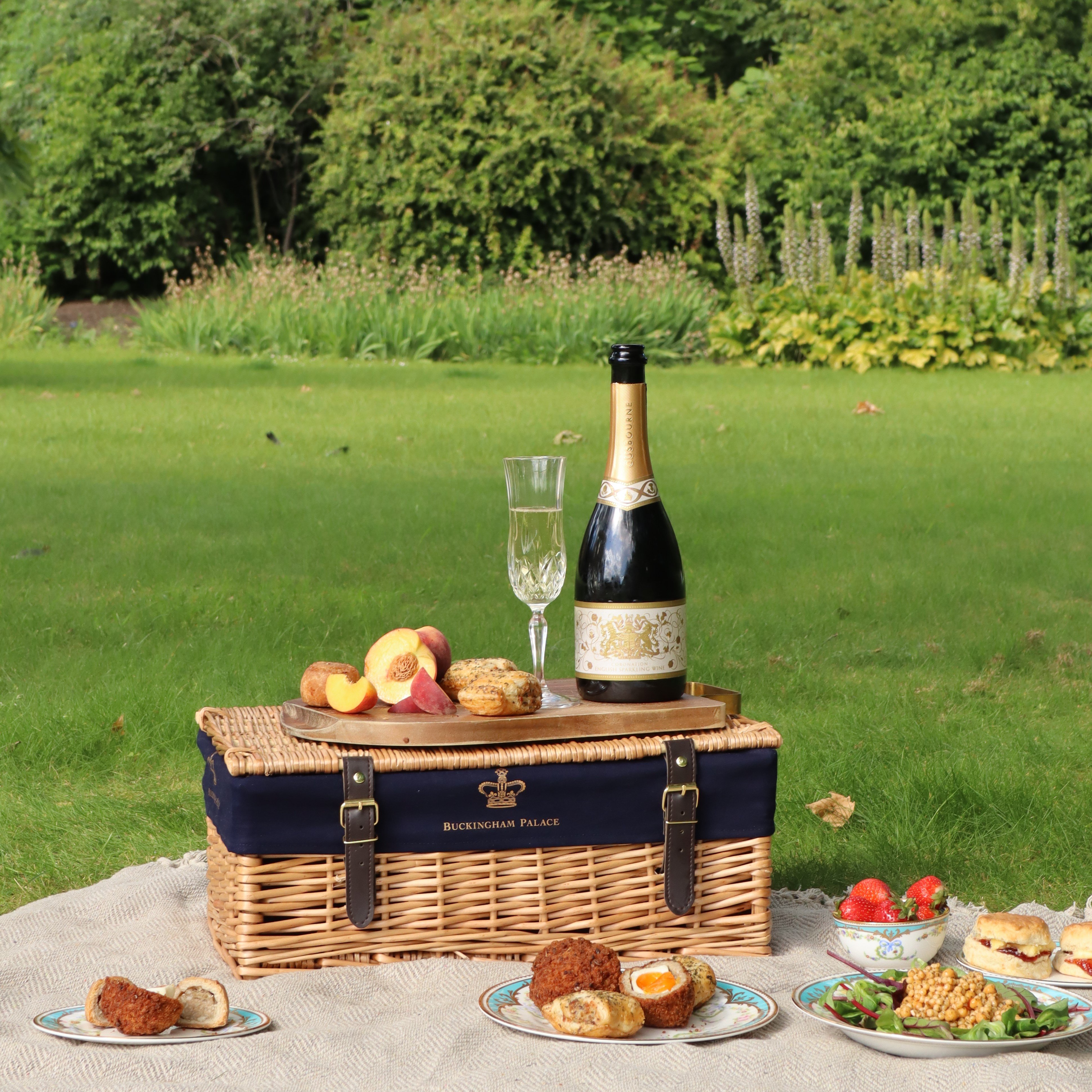 A picnic hamper with a variety of small plates and fruit displayed around it